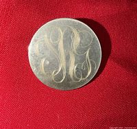 front of circular silver-tone brooch showing engraved script monogram