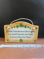 Front view of ceramic plaque showing quote, shamrocks, rope hanger, ruler for scale
