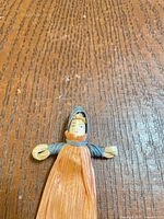 Front view of corn husk doll bookmark showing face, orange body, grey hood and arms