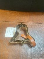 Three nested gold-tone bell cookie cutters with leather strap