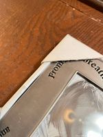 Corner of silver metal frame showing protective cardboard and part of inscription