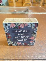 Front view of wooden block sign showing floral design and phrase