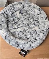 Top view of grey faux-fur round pet bed with attached brand tag