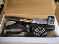 Open box showing scrubber handle, extension shaft and several brush heads