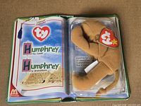 Opened book-style package showing Humphrey the Camel Beanie inside blister