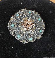 Front view of round silver brooch with turquoise accents and raised rose center