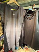 Two Under Armour tank tops hanging, full view of both items