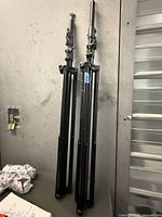 Two black metal tripod stands folded and leaning against a wall