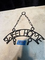 Front view of cast iron “SWEET HOME” key holder showing three hooks and hanging chain