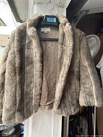 Front view of brown faux fur jacket on hanger showing lining and exterior