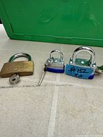 Three padlocks laid on tabletop: brass padlock left, two smaller laminated steel padlocks right, keys visible