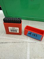 Closed red case holding steel letter punches with lid beside it