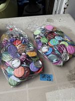 Two plastic bags filled with assorted coloured pin-back buttons
