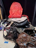Pile of purses showing red mini backpack, matching wristlet, grey and olive bags, brown crocodile-embossed satchel