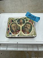 Top view of rectangular antique tin showing lithographed portraits and wear