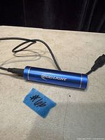 Blue Bud Light cylindrical power bank connected to USB charging cable, ID tag visible