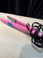 Side view of pink Conair hair straightener showing ceramic plates and black cord