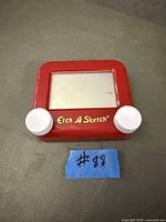 Front view of red mini Etch A Sketch showing screen, knobs and branding