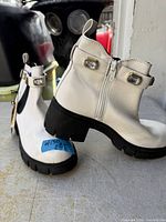 Full view of both boots showing off-white uppers, rhinestone strap, inner zipper, black lug soles