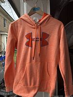 Front view of orange Under Armour ladies pullover hoodie on hanger