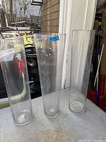 Three tall clear glass cylinder vases standing on table