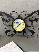 Front view of black metal butterfly wall clock on surface