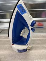 Right side view of blue and white Proctor Silex steam iron standing upright, shows steam control knob and water fill opening.