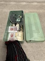 Open green box showing interior hardware, attachments, needle packs and fabric sample