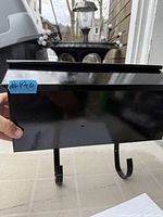 Front view of black metal wall-mount mailbox with glossy finish and bottom hooks