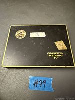 Top view of Player's Navy Cut black tin showing logo, text, wear, sticker residue