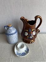 Front view of all three ceramics: copper luster pitcher, speckled jug, egg cup on saucer
