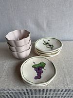 Stack of four scalloped bowls and small plates with grape and olive designs