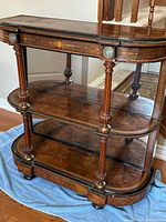 Front view of three-tier burl walnut console table with mirrored back and brass accents