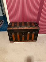 Front view of antique dome-top steamer trunk showing wood slats and metal hardware