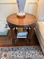 Full view of round carved wood table with barley twist legs and lower shelf beside sofa