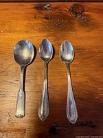 Front view of three assorted sterling spoons, handles showing patterns