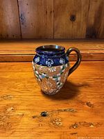 Front view of the stoneware jug showing cobalt blue collar, floral slip decoration, brown handle