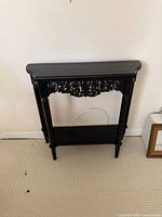 Front angled view of black console table showing carved apron and lower shelf