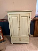 Front view of cream distressed armoire showing doors and drawers