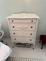 Front view of cream painted 4-drawer chest showing hardware and turned legs on casters