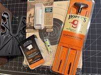 All listed shotgun cleaning items laid out including Hoppe's rod kit, BoreSnake, bore brush, repair tape, target, plastic gun rest