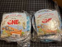 front view of two sealed bundles showing napkin graphic and plates behind