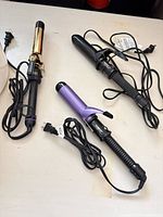 All three curling irons with cords displayed on tabletop