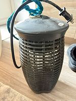 Full view of black cylindrical bug zapper with cord, plug and hanging rope