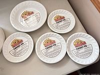 Five identical ceramic pie plates displayed; top view shows recipe graphic and rim design