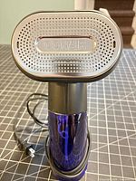 Front view of Conair handheld garment steamer showing silver perforated faceplate with logo and blue reservoir