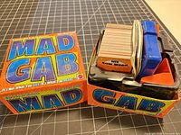 Closed Mad Gab box with lid removed showing cards, timer, score pad and components inside
