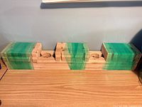 Front view of three plastic-wrapped wine rack tiers showing bottle cut-outs and dowel holes