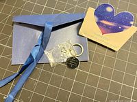 Keychain, blue envelope, ribbon, and thank-you card displayed on cutting mat