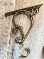 First bracket showing scroll design and mounting rail, hardware bag visible